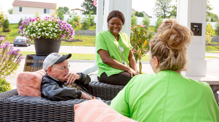 senior man on patio laughing with group of caregivers in green