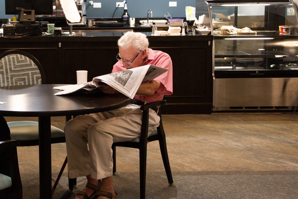 senior reading the newspaper while enjoying a cup of coffee at the cafe of a senior living community