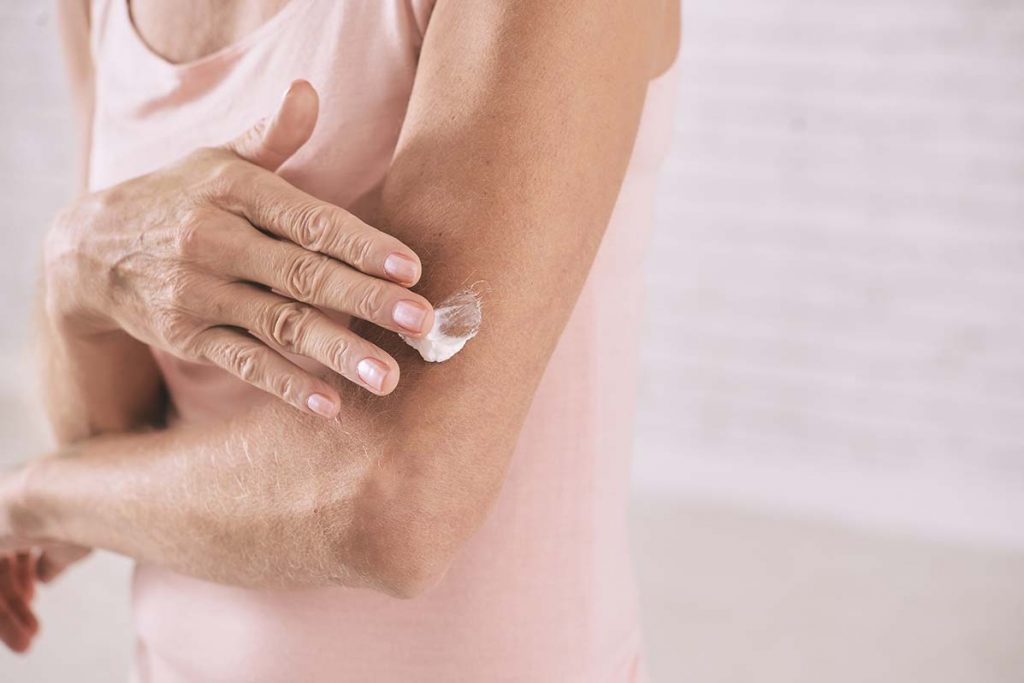 Women practicing summer safety tips by applying sunscreen onto her arms before heading out to enjoy the summer air