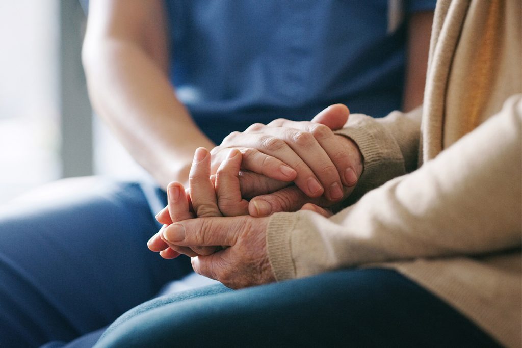 Adult child and mother holding hands and sitting next to each other