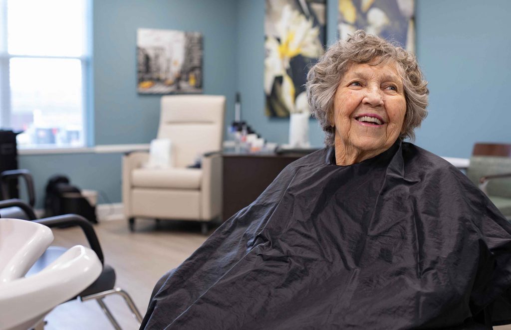Senior living resident smiling while getting her hair done at the salon within the StoryPoint community.