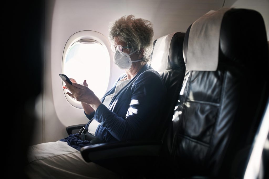 senior seated on an airplane with a mask and reading a bout travel tips for seniors