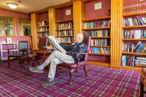 senior reading newspaper in library