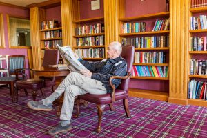 senior man reading newspaper in a library