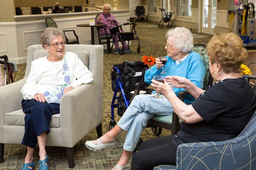 Three Independence Village senior residents enjoying some cocktails and chatting in the lounge area at their senior living community