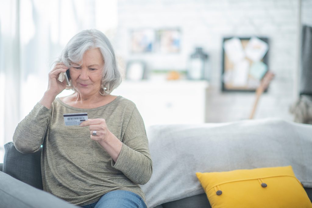 Senior woman looking at her credit card while on the phone