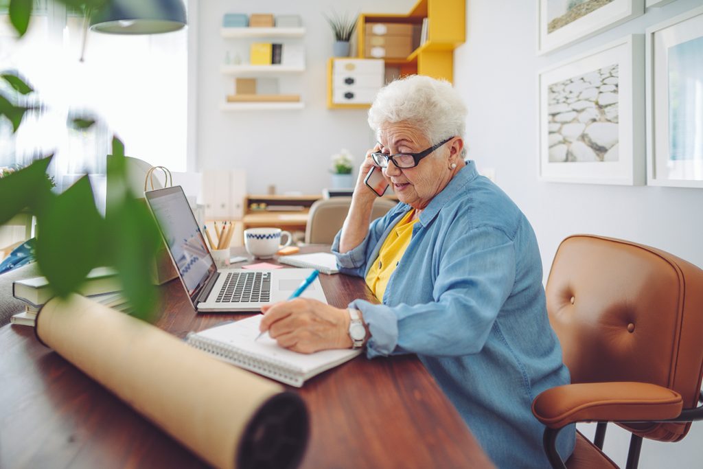 woman on the phone while taking notes about common senior scams