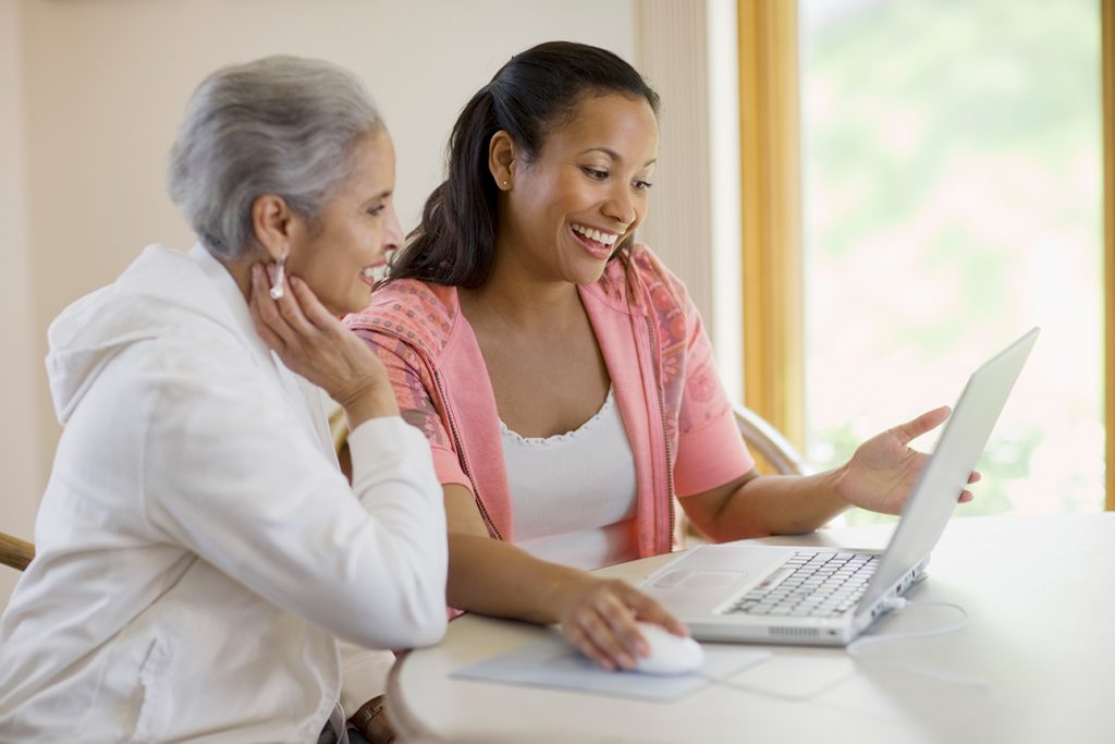 adult daughter teaching her loved one how to use a video chat device to video call her friends and family