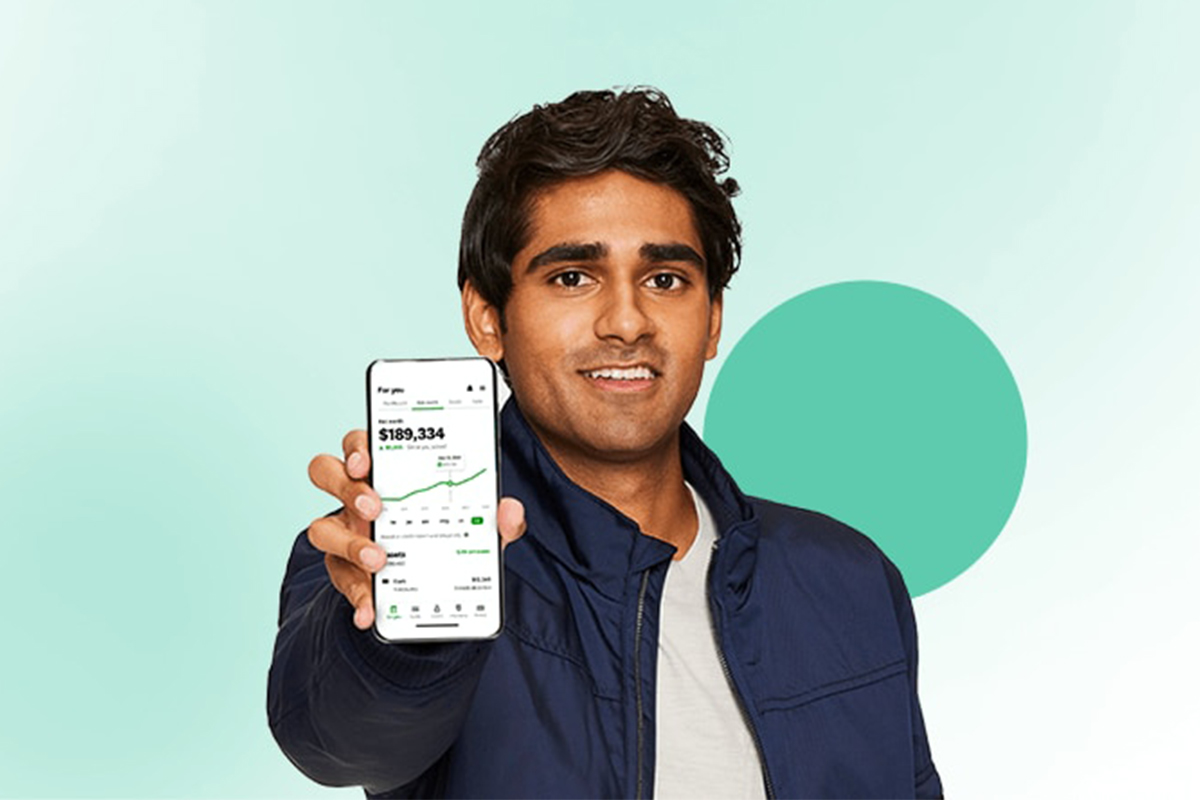 A man holding out a smartphone so that the viewer can see the screen, showing a financial app with a line graph trending upward. 