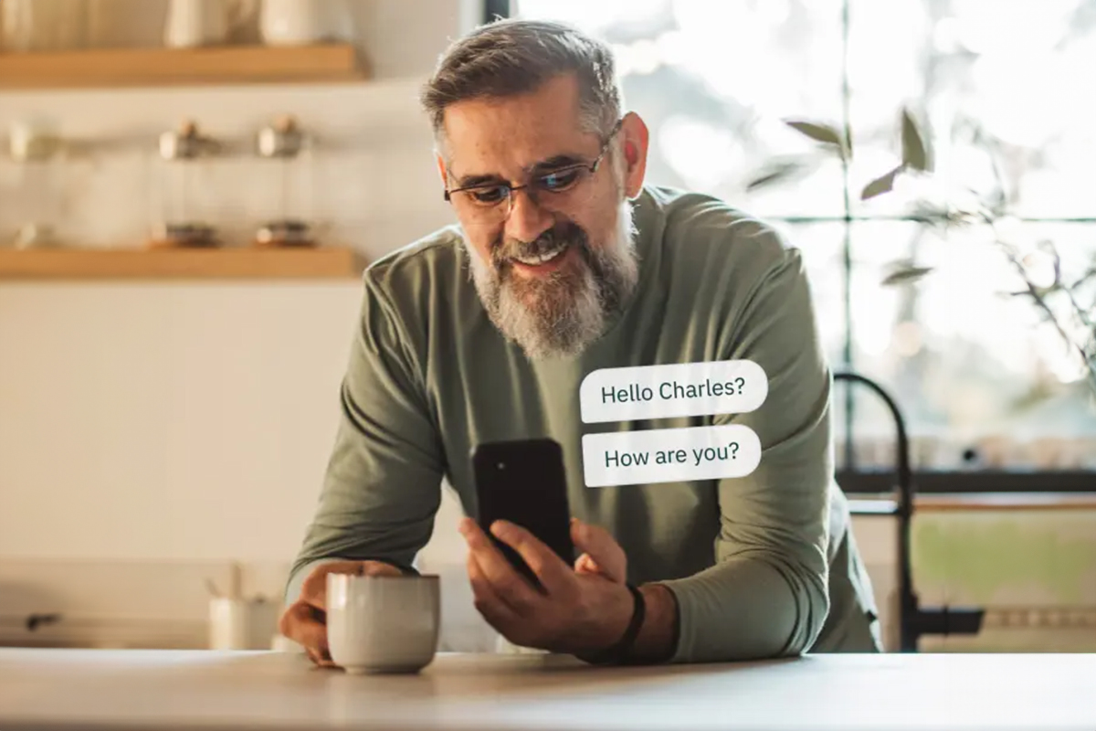 A senior man in his kitchen looking at a smart phone, with text bubbles showing that he has received messages. 