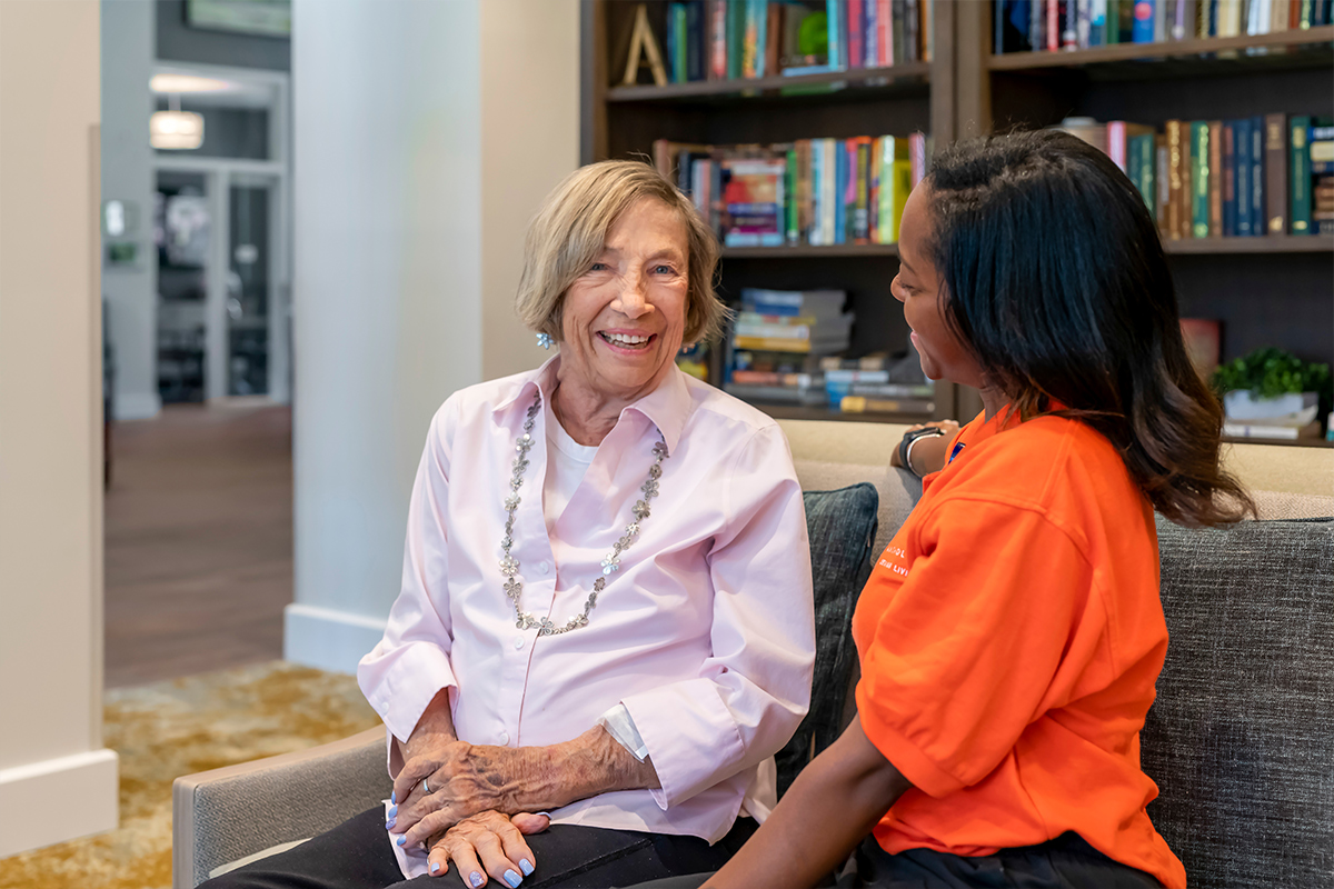 Memory care resident and their caregiver smiling together in a library.