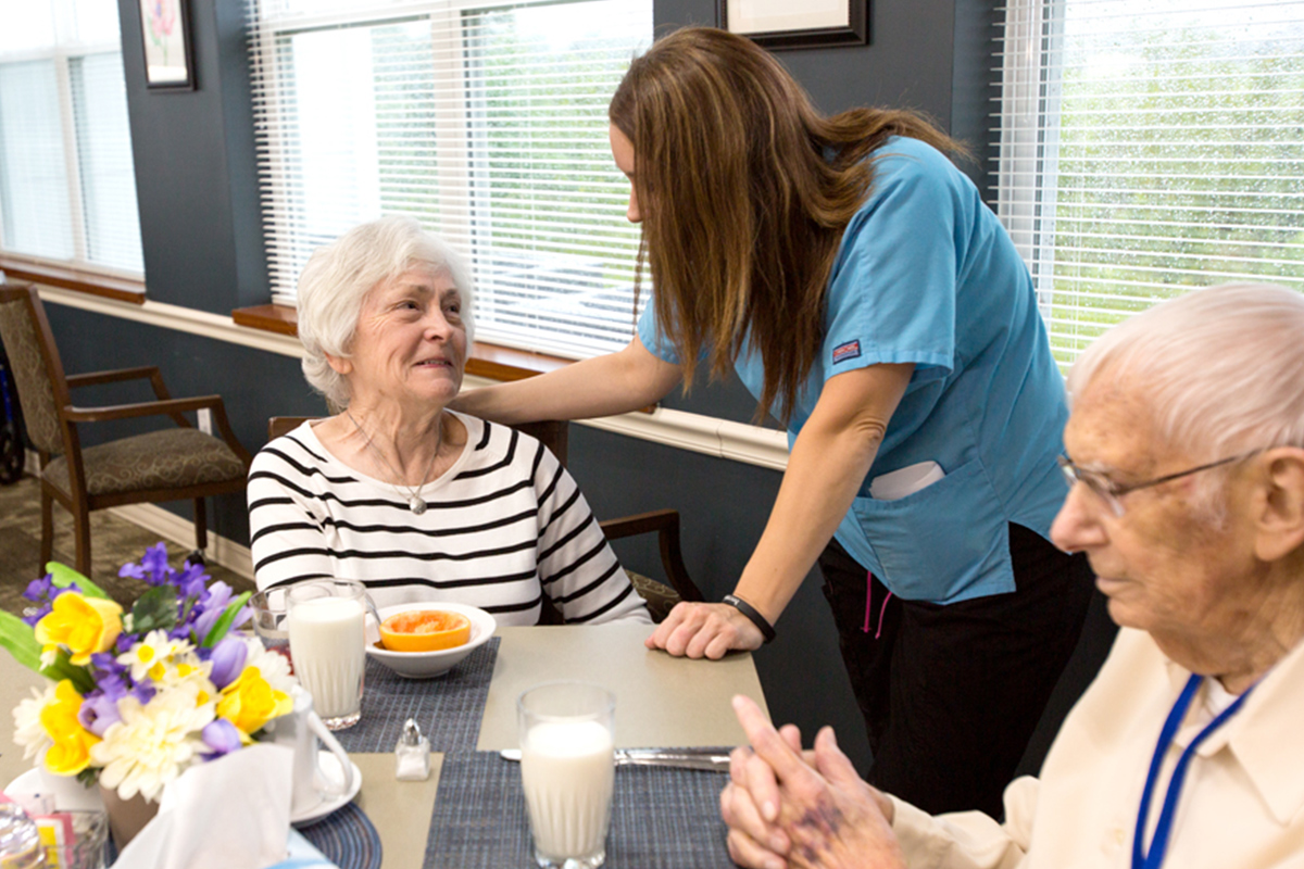 StoryPoint Group residents enjoying a meal in the dining room and speaking to a caregiver. 