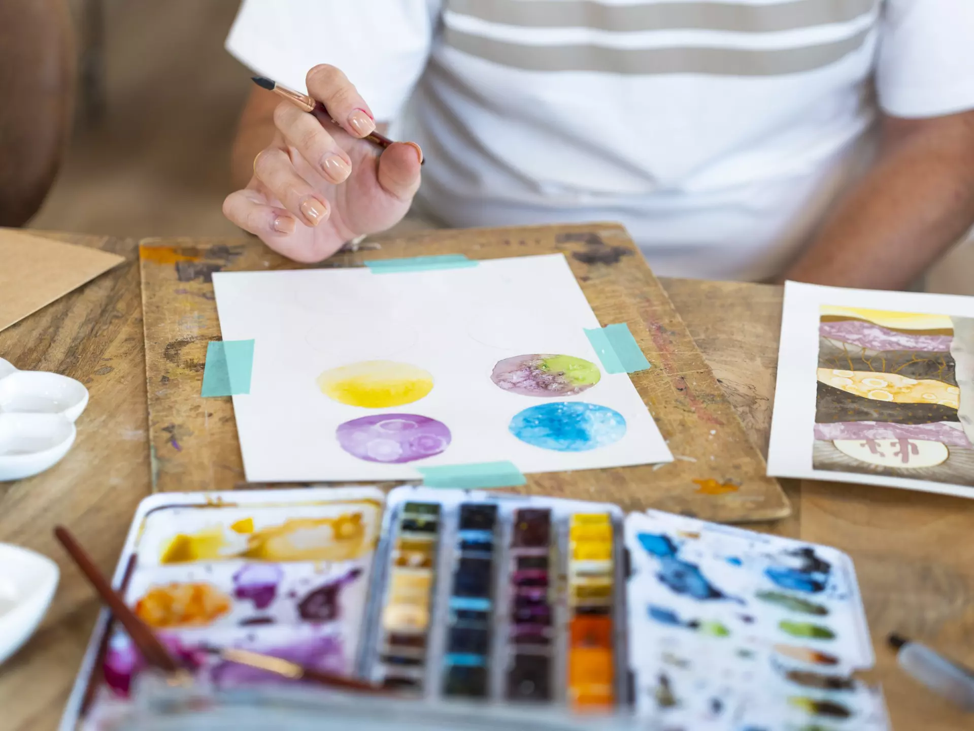 A senior woman using watercolor paints, creating images of circular shapes on her paper.
