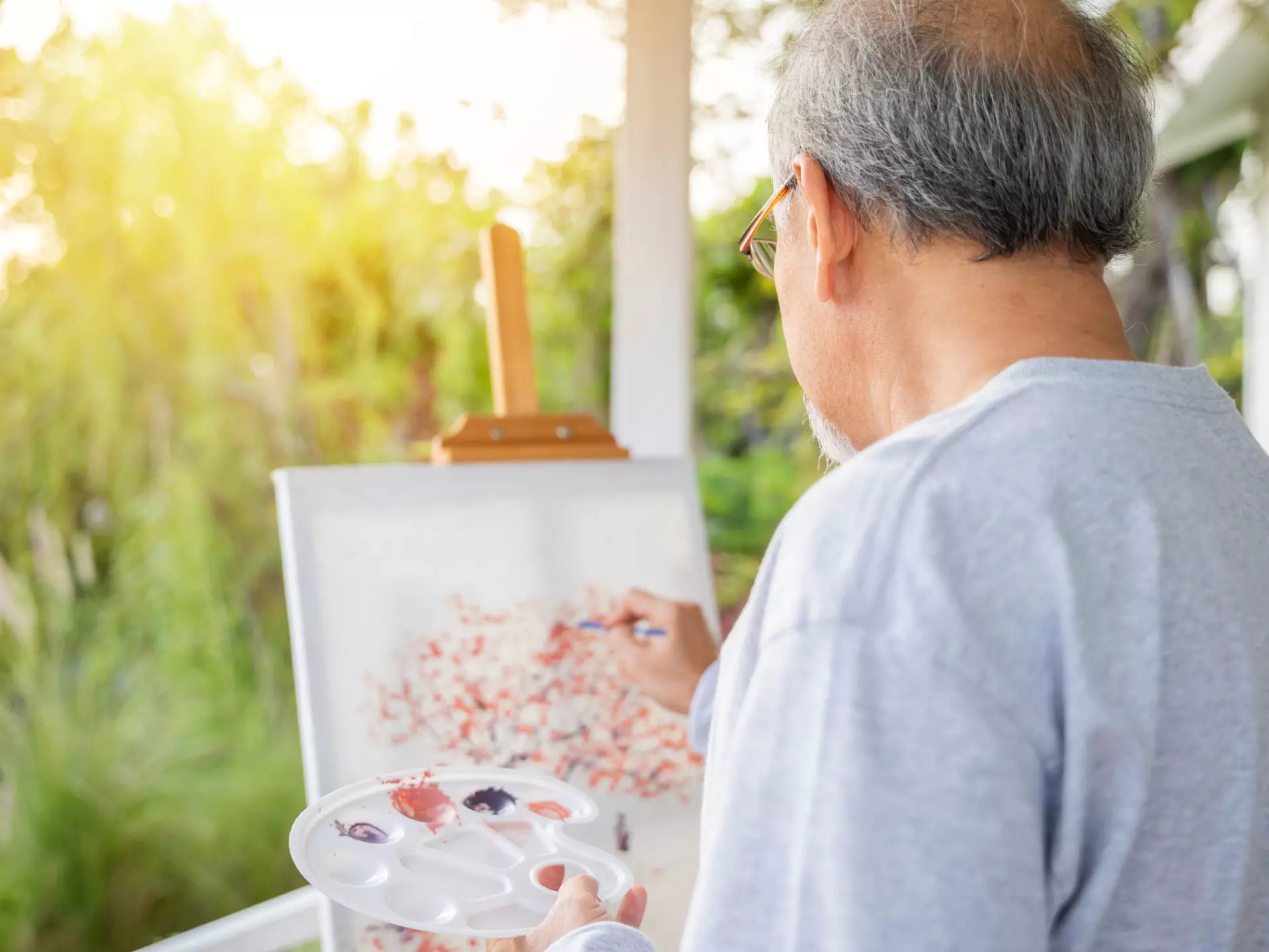 A senior man painting outside on a porch.