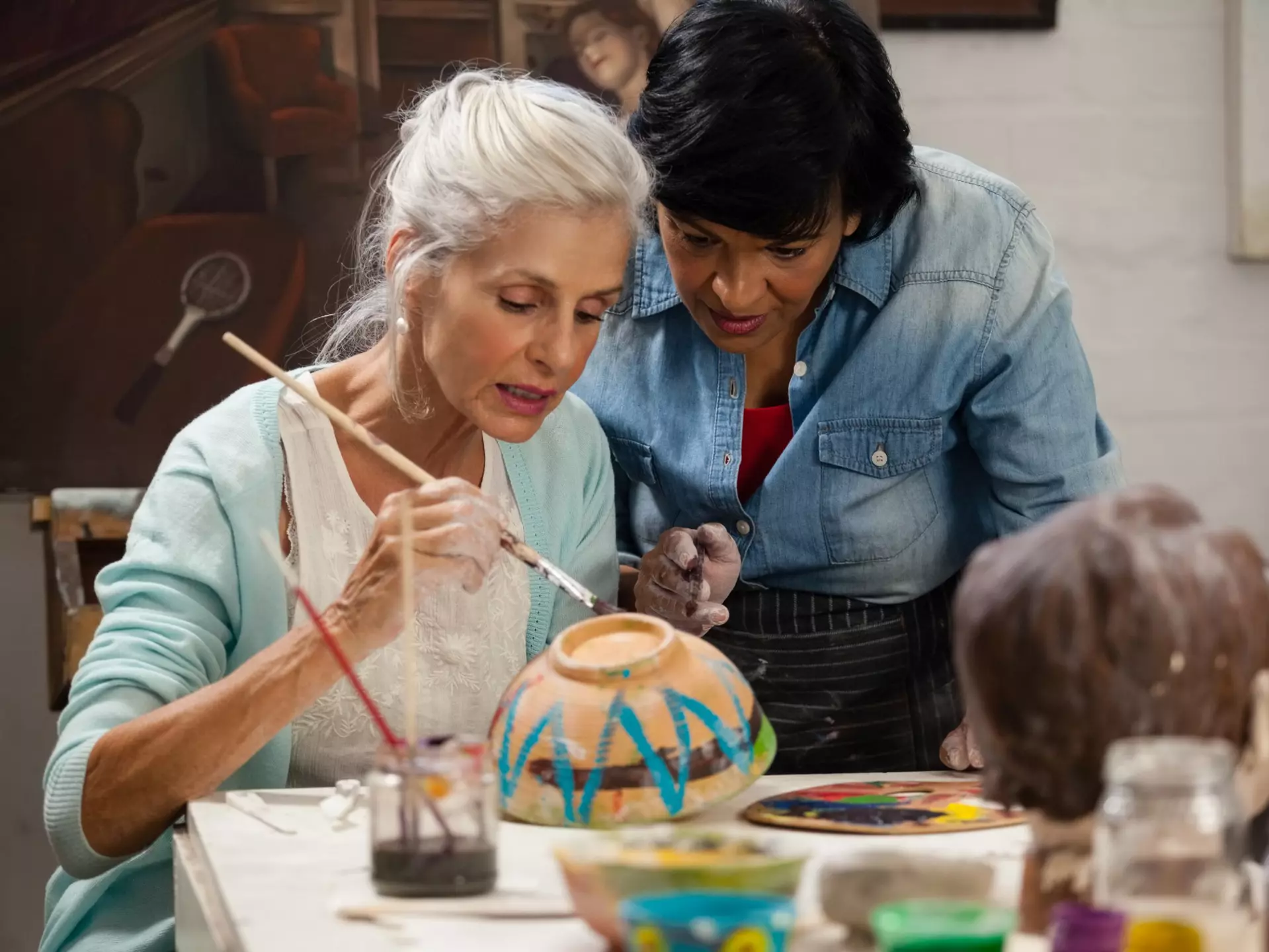 A senior and her art therapist are working together to paint a pottery bowl.