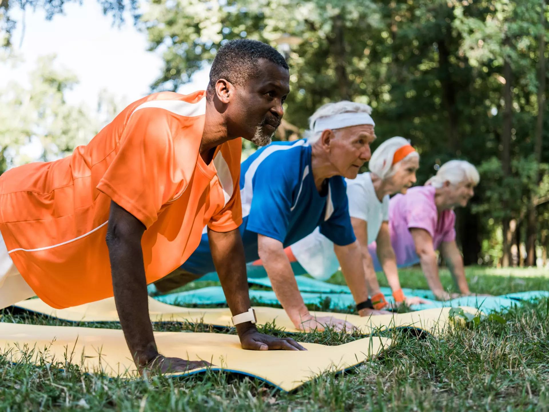 selective focus of senior african american man doing plank exercise with other seniors on fitness mats