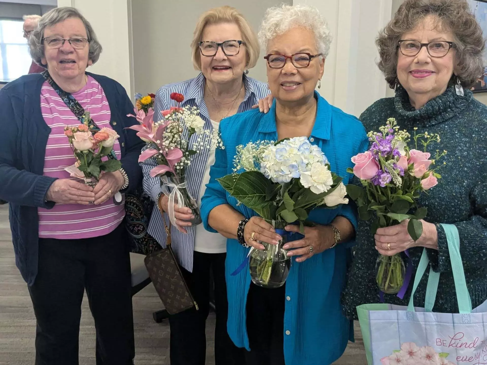 Happy StoryPoint Group residents are standing in a group, holding bouquets of flowers.