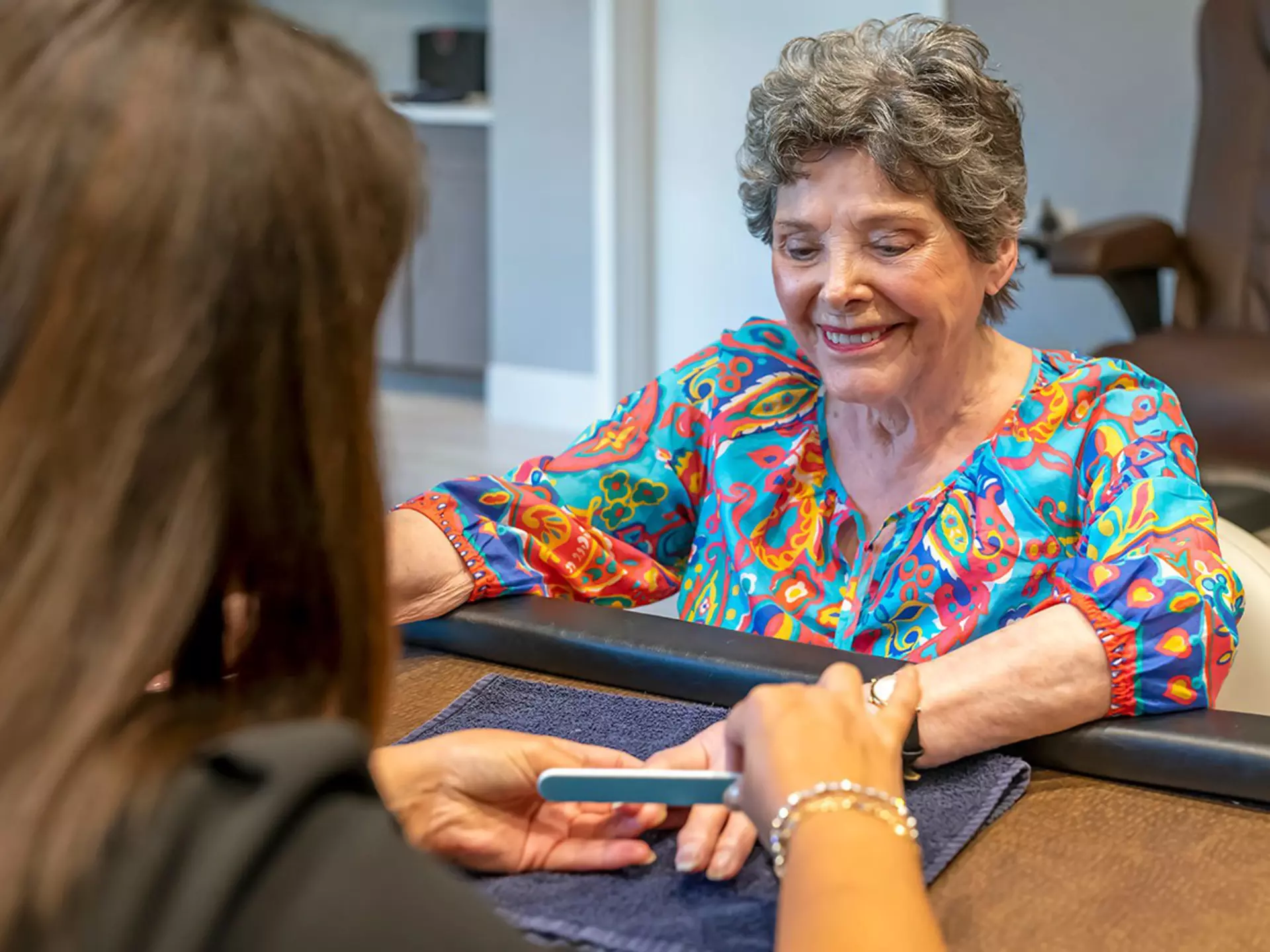 A happy senior woman is receiving a manicure at a salon.