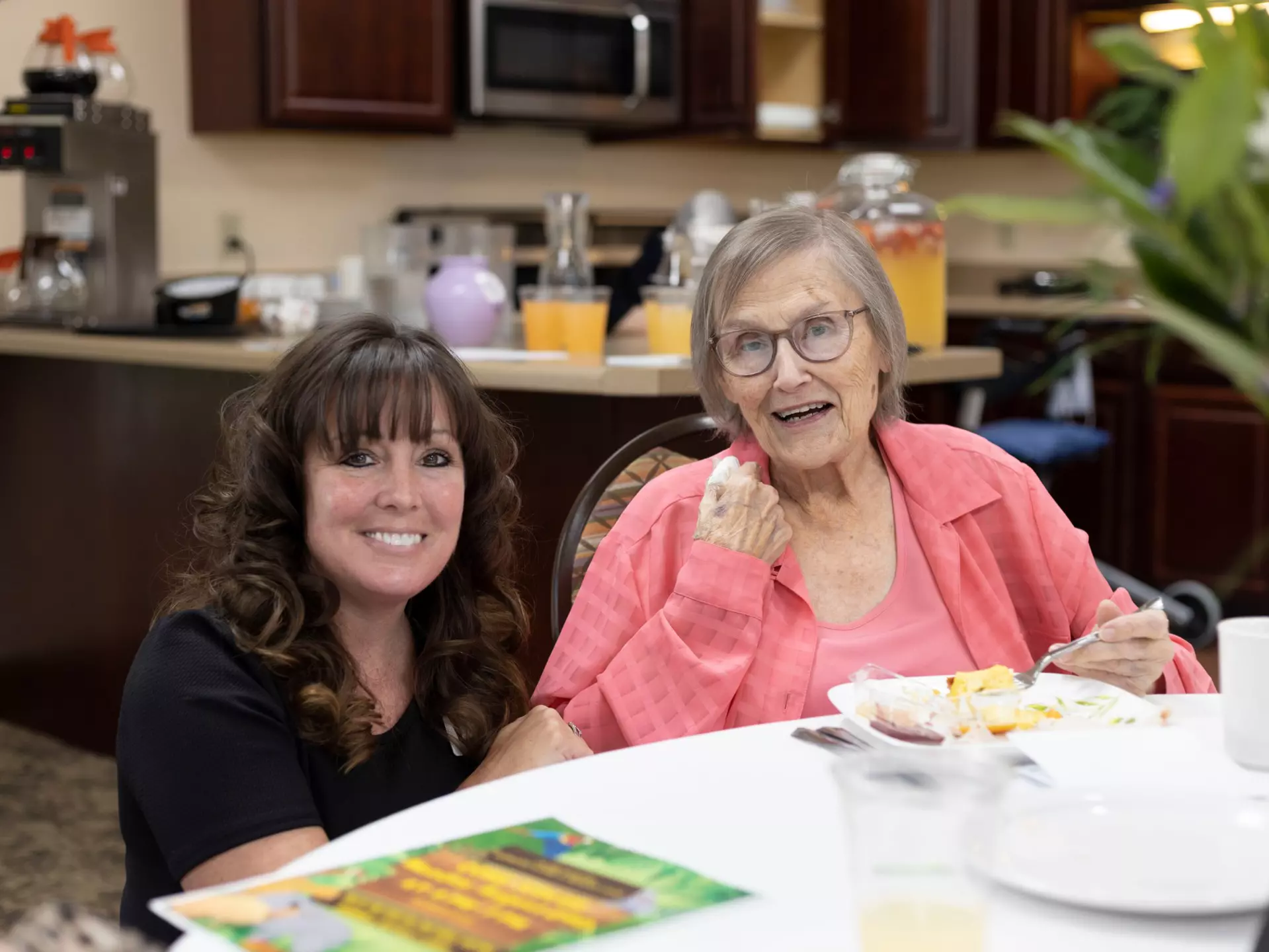 A senior woman and a caregiver pose for a photo in the dining room of a senior living community.