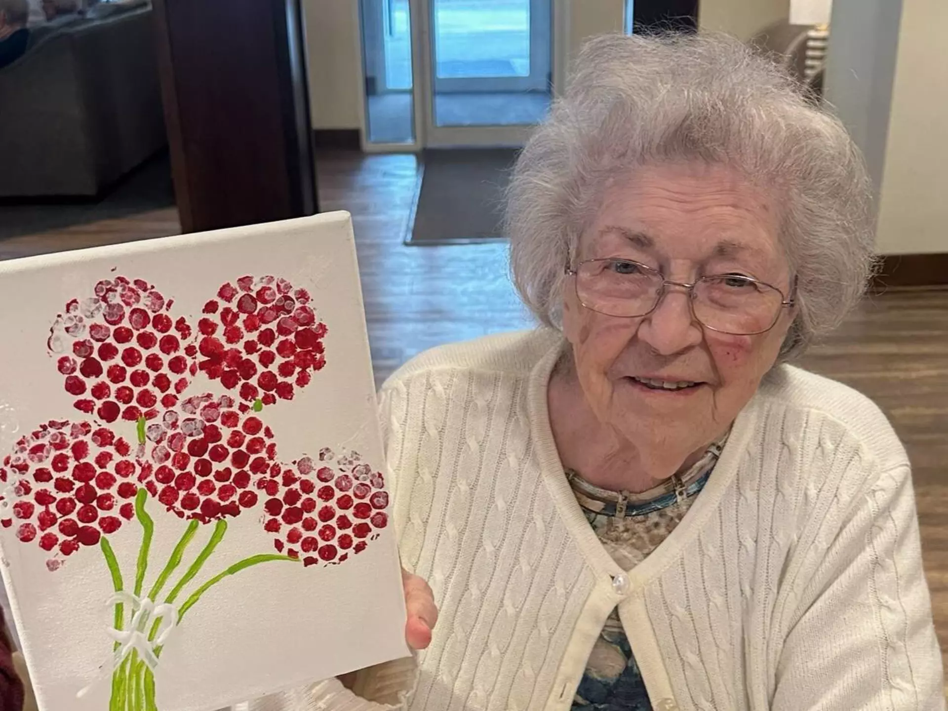 A smiling senior woman is showing off her artwork. 