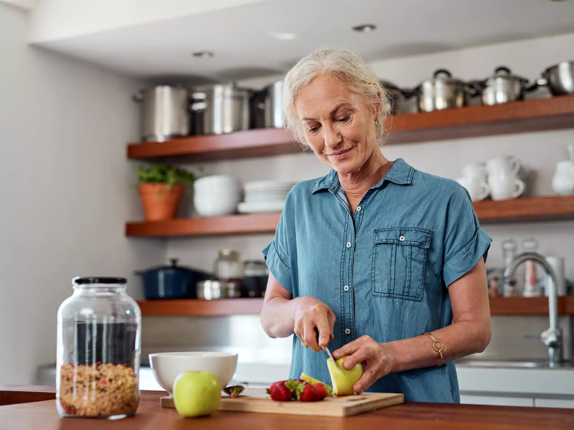A senior woman is cutting up an apple in the kitchen.