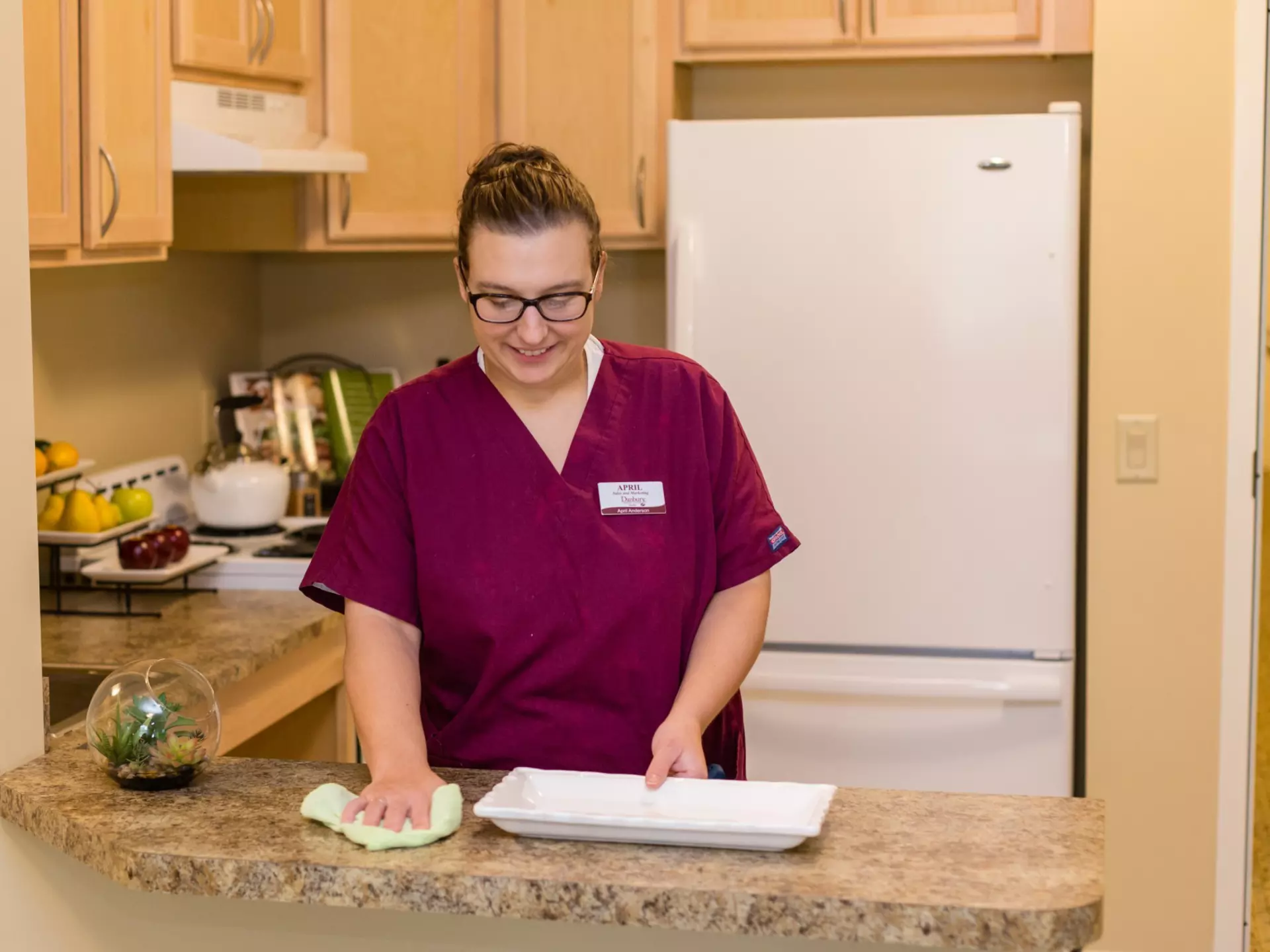 A caregiver is wiping down the kitchen counters in a senior's apartment.